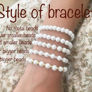 Puede incluir: Cinco pulseras de perlas blancas con diferentes estilos. Las pulseras est&aacute;n apiladas en la mu&ntilde;eca de una persona. La pulsera superior no tiene cuentas met&aacute;licas, la segunda pulsera tiene cuentas plateadas, la tercera pulsera tiene cuentas doradas, la cuarta pulsera tiene cuentas plateadas m&aacute;s grandes y la quinta pulsera tiene cuentas doradas m&aacute;s grandes.