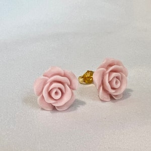 Op de afbeelding: Een paar roze rozenbloem oorbellen. De oorbellen zijn gemaakt van glad, gepolijst materiaal en hebben een delicaat, vrouwelijk ontwerp.