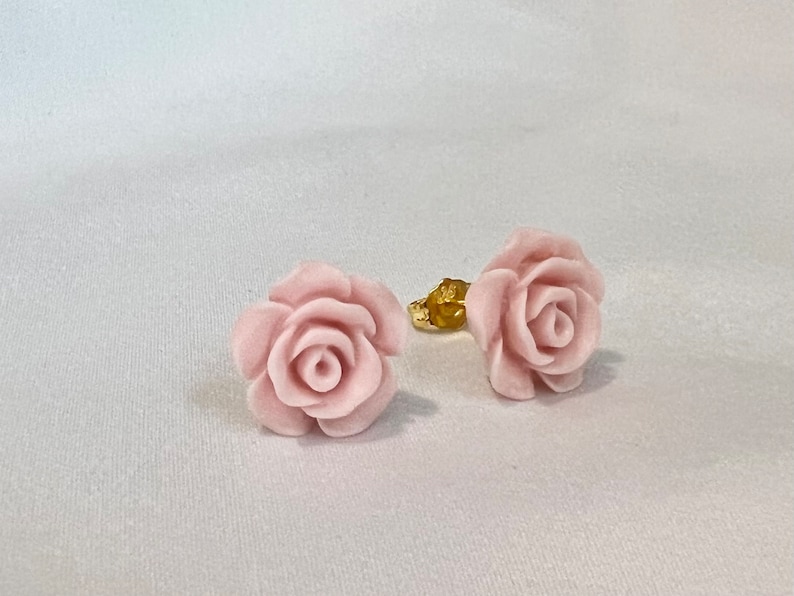 Op de afbeelding: Een paar roze rozenbloem oorbellen. De oorbellen zijn gemaakt van glad, gepolijst materiaal en hebben een delicaat, vrouwelijk ontwerp.