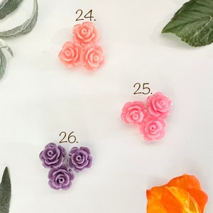 May include: Three pink plastic rose flower embellishments, three pink plastic rose flower embellishments, and three purple plastic rose flower embellishments.