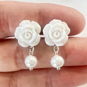 Op de afbeelding: Een paar witte rozenbloem oorbellen met een parel die aan elke bloem hangt.