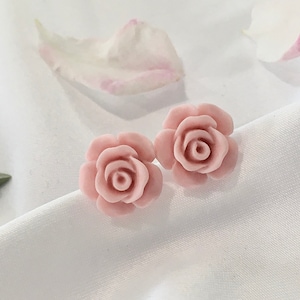 Op de afbeelding: Een paar roze roosvormige oorbellen. De oorbellen zijn gemaakt van een glad, lichtroze materiaal en hebben een delicaat, vrouwelijk ontwerp.