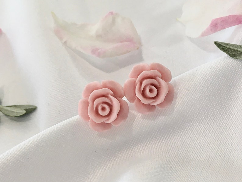 Op de afbeelding: Een paar roze roosvormige oorbellen. De oorbellen zijn gemaakt van een glad, lichtroze materiaal en hebben een delicaat, vrouwelijk ontwerp.
