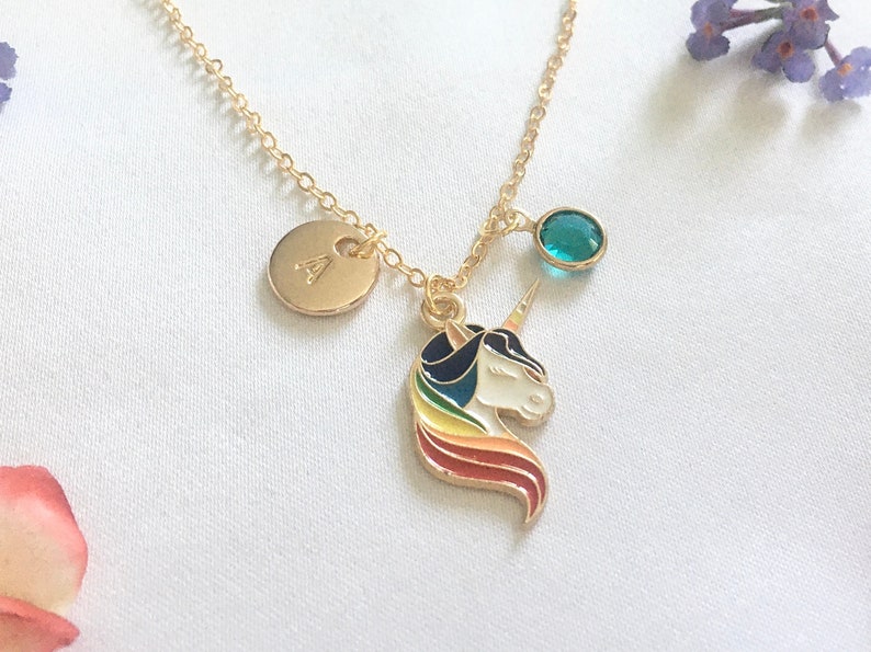 May include: Gold necklace with a unicorn charm, a small round charm with the letter 'A' and a teal blue gemstone. The unicorn charm has a rainbow mane and tail.