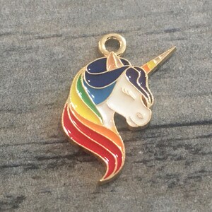 May include: Gold-tone metal charm featuring a unicorn head with a rainbow mane and horn. The unicorn is white with a blue mane and a yellow horn.