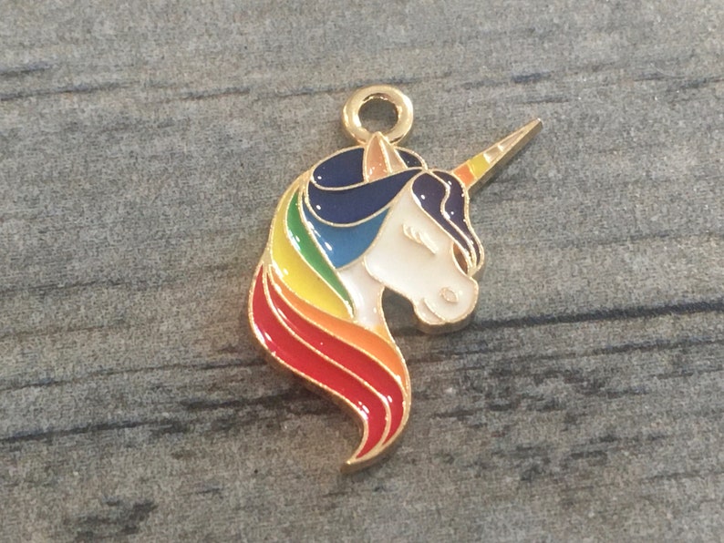 May include: Gold-tone metal charm featuring a unicorn head with a rainbow mane and horn. The unicorn is white with a blue mane and a yellow horn.