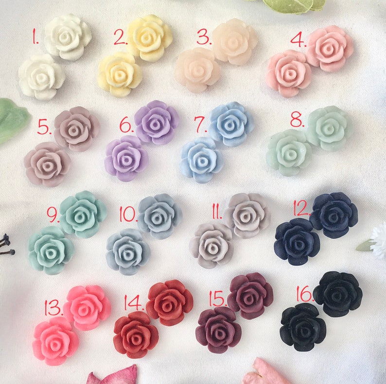 Op de afbeelding: Assortiment van 16 kleine, decoratieve, hars rozenbloem versieringen in verschillende kleuren, waaronder wit, roze, lavendel, blauw, grijs, rood en zwart. Elke roos is genummerd van 1 tot 16.