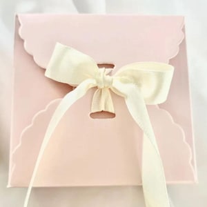 May include: A pink gift box with a scalloped edge and a white satin ribbon tied in a bow.