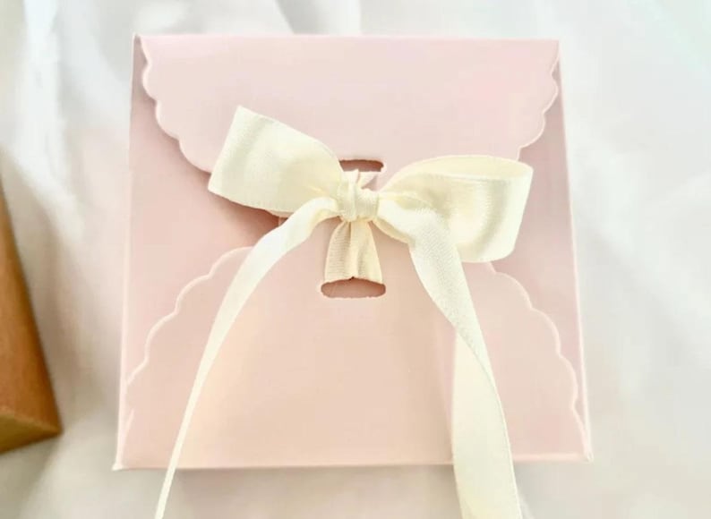 May include: A pink gift box with a scalloped edge and a white satin ribbon tied in a bow.