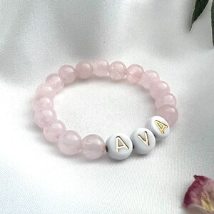 May include: A pink beaded bracelet with the name "AVA" spelled out in white beads with gold lettering.