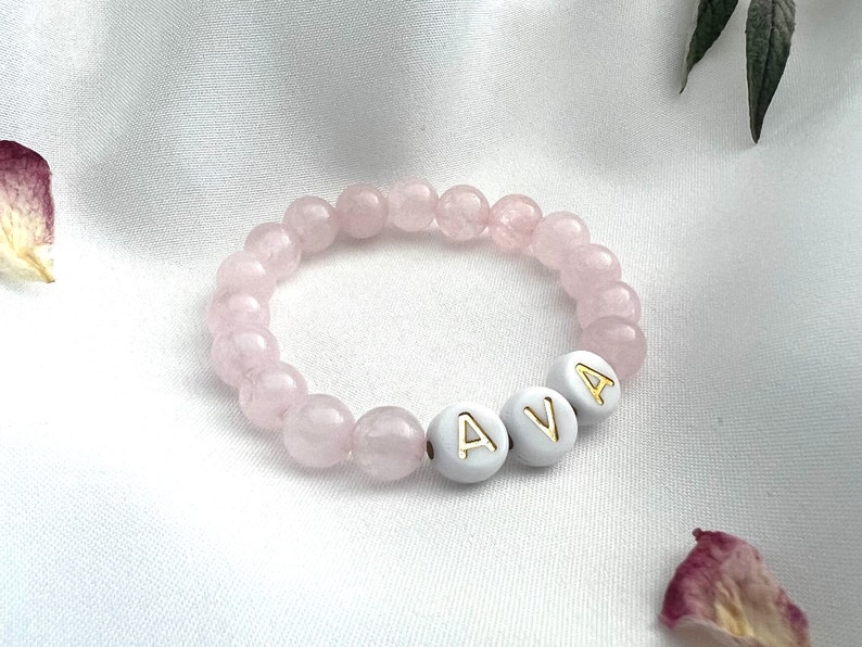 May include: A pink beaded bracelet with the name "AVA" spelled out in white beads with gold lettering.