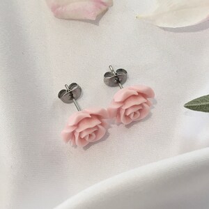 Op de afbeelding: Een paar zilveren oorbelletjes met roze rozenbloem accenten. De oorbelletjes liggen op een witte achtergrond.