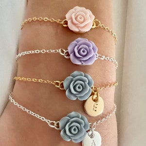 May include: Four delicate bracelets with silver and gold chains. Each bracelet features a different colored flower charm, including pink, purple, gray, and a silver charm with the letter 'E' and a gray charm with the letter 'A'.