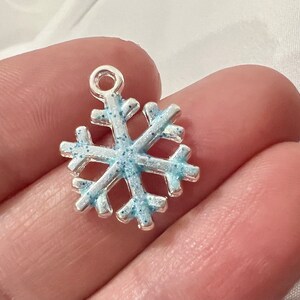 May include: A silver snowflake charm with blue glitter accents. The snowflake is a popular holiday decoration and can be used for jewelry making, scrapbooking, and other crafts.