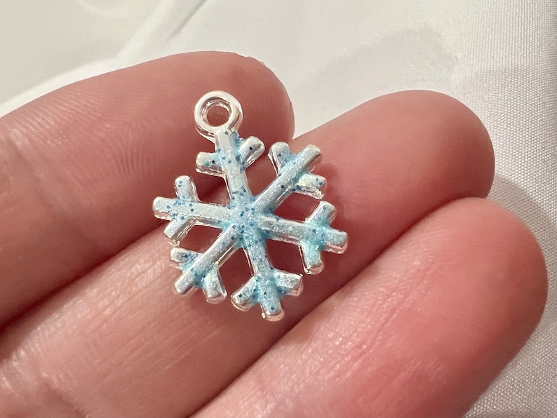 May include: A silver snowflake charm with blue glitter accents. The snowflake is a popular holiday decoration and can be used for jewelry making, scrapbooking, and other crafts.