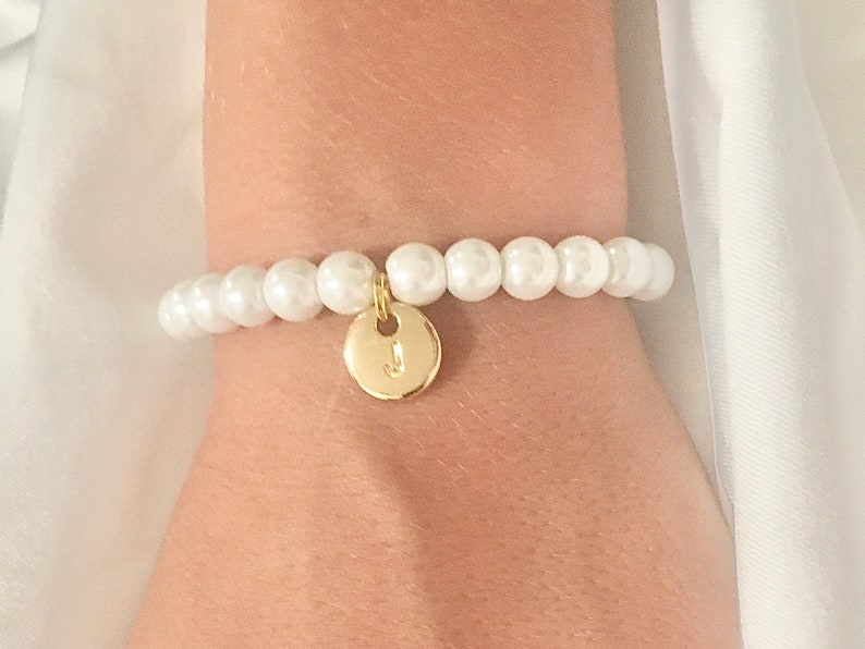 May include: A white pearl bracelet with a gold charm featuring the letter "J".