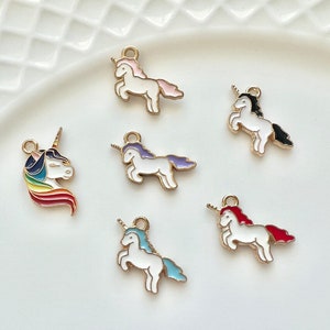 May include: Six gold-tone unicorn charms with enamel details. Each charm features a white unicorn with a different colored mane and tail. The charms are perfect for adding a touch of whimsy to jewelry or crafts.