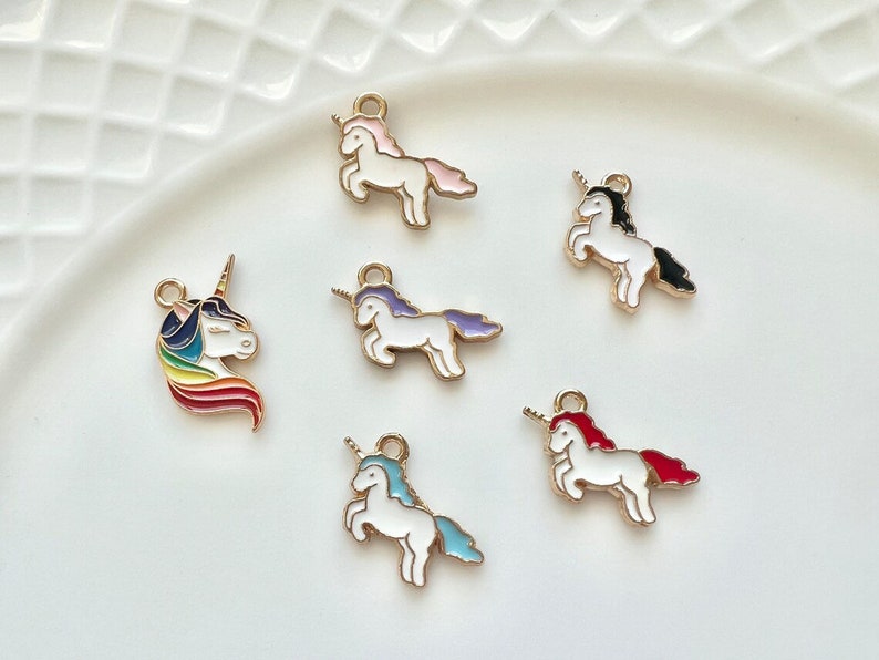 May include: Six gold-tone unicorn charms with enamel details. Each charm features a white unicorn with a different colored mane and tail. The charms are perfect for adding a touch of whimsy to jewelry or crafts.