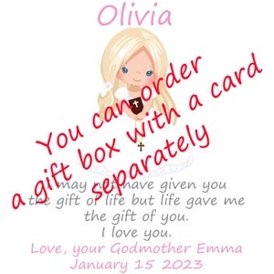 May include: A white card with a pink and white illustration of a girl in a white dress holding a book. The text "Olivia" is at the top of the card. The text "You can order a gift box with a card separately" is written in red and white on the card. The text "may have given you the gift of life but life gave me the gift of you. I love you." is written in black. The text "Love, your Godmother Emma January 15 2023" is written in pink at the bottom of the card.