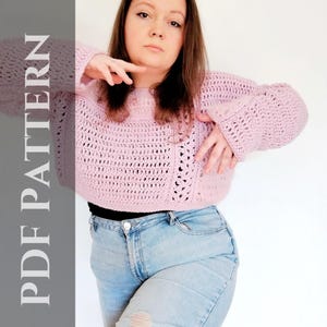 Könnte beinhalten: Ein rosa gehäkelter Pullover mit lockerer Passform und langen Ärmeln. Der Pullover ist verkürzt und hat ein zartes Lochmuster.