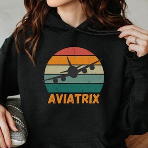 May include: Black hoodie with a vintage-style sunset graphic featuring a silhouette of an airplane and the text "AVIATRIX".