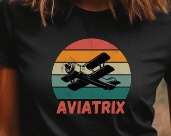 May include: Black t-shirt with a vintage-style graphic of a plane flying in front of a sunset. The text "AVIATRIX" is printed below the graphic.