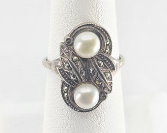 May include: A silver ring with two white pearls and a marcasite design.