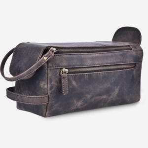 May include: A distressed brown leather toiletry bag with two zippered compartments and a small handle. The bag has a rectangular shape with a curved handle on one side and a small flap on the other.