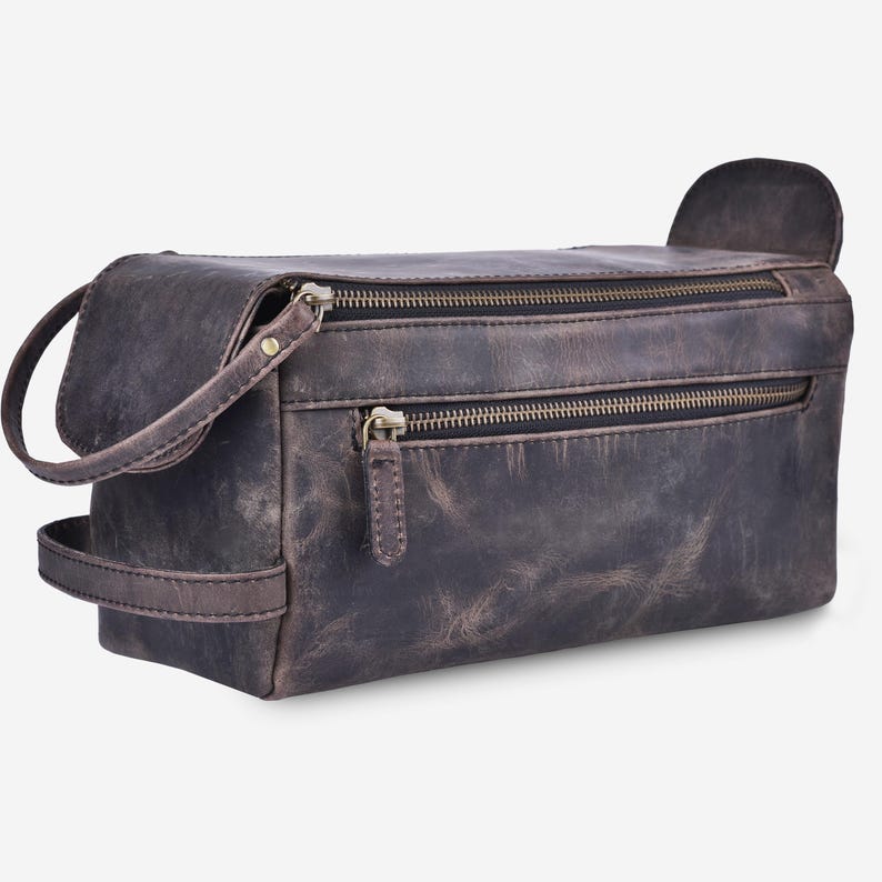 May include: A distressed brown leather toiletry bag with two zippered compartments and a small handle. The bag has a rectangular shape with a curved handle on one side and a small flap on the other.