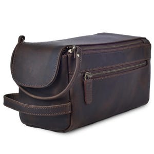 May include: A brown leather toiletry bag with multiple zippered compartments. The bag has a handle on the side and a curved flap on top. The leather has a distressed appearance.