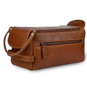 May include: A brown leather toiletry bag with two zippered compartments and a small handle. The bag has a rectangular shape with rounded edges and a flap closure on one side. The zippers and hardware are a dark bronze color.