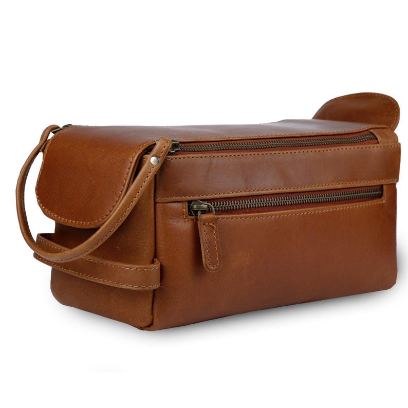 May include: A brown leather toiletry bag with two zippered compartments and a small handle. The bag has a rectangular shape with rounded edges and a flap closure on one side. The zippers and hardware are a dark bronze color.