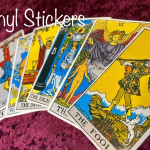 May include: Vinyl stickers featuring images of tarot cards, including The Fool, The High Priestess, Death, and The Magician. The cards are arranged in a fan shape on a burgundy velvet surface.