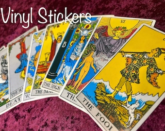 May include: Vinyl stickers featuring images of tarot cards, including The Fool, The High Priestess, Death, and The Magician. The cards are arranged in a fan shape on a burgundy velvet surface.