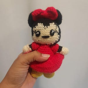 Op de afbeelding: Gehaakte Minnie Mouse pop. De pop heeft een rode jurk, een rode strik, zwarte oren en gele schoenen. De pop is handgemaakt en heeft een lachend gezicht met grote ogen.