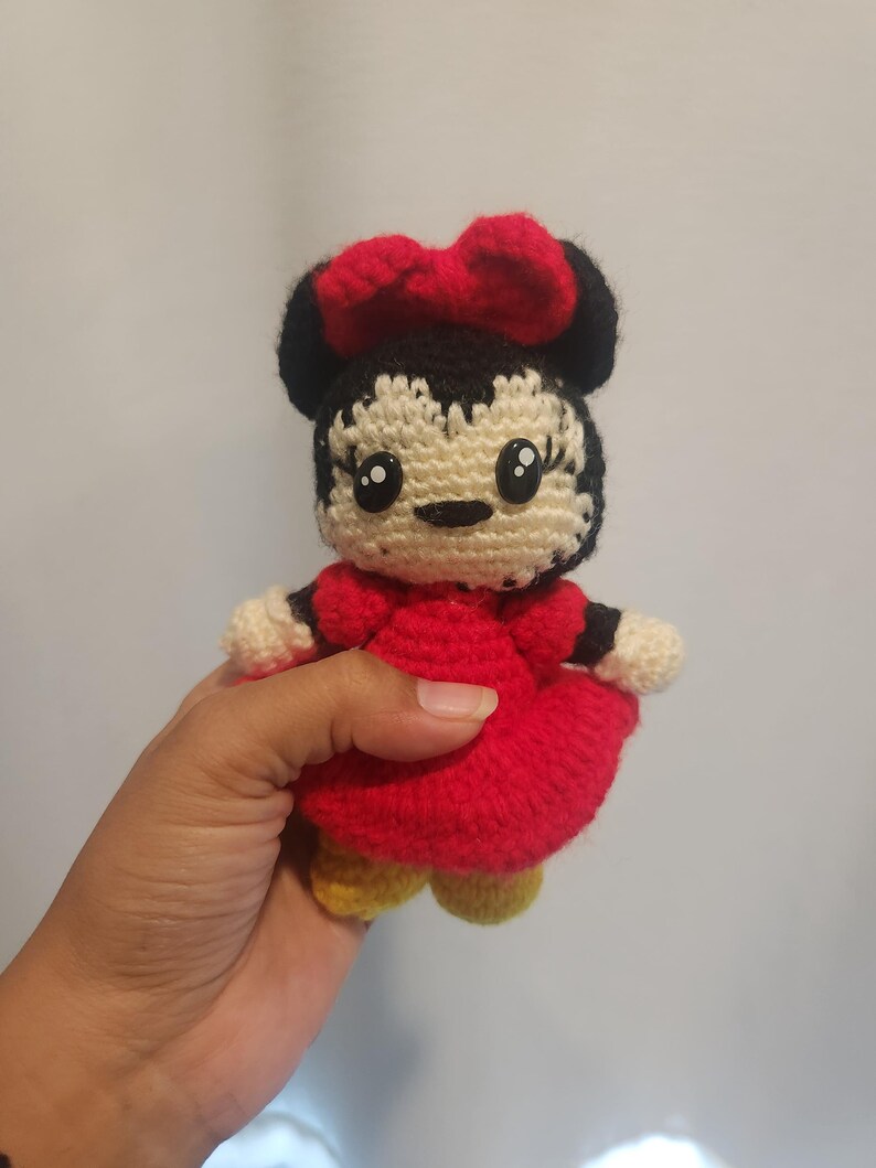 Op de afbeelding: Gehaakte Minnie Mouse pop. De pop heeft een rode jurk, een rode strik, zwarte oren en gele schoenen. De pop is handgemaakt en heeft een lachend gezicht met grote ogen.