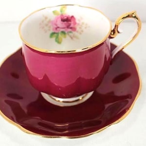 Puede incluir: Juego de taza y platillo de té burdeos con ribete dorado. La taza presenta un diseño floral en el interior. El juego es de porcelana con acabado brillante. El asa de la taza es dorada.