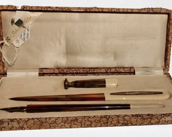 Op de afbeelding: Een bruine houten doos met een wit interieur, met een set van drie schrijfbenodigdheden: een pen, een briefopener en een zegellak. De doos is gevoerd met een bruin, gepatenteerd stof.
