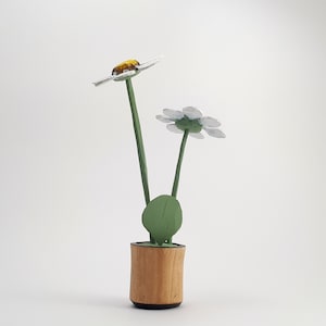 May include: Two white wooden daisies in a brown wooden pot with a green leaf. The daisies are painted white with yellow centers.