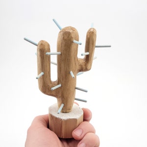 May include: A wooden cactus sculpture with light blue painted spines. The cactus is standing on a wooden base.