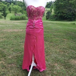 May include: A pink satin and lace formal gown with a sweetheart neckline and a high slit. The gown has a beaded embellishment at the waist.