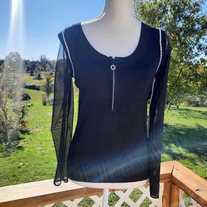 May include: Black long-sleeved shirt with a zipper and a mesh overlay. The shirt has a scoop neck and is decorated with a row of rhinestones.