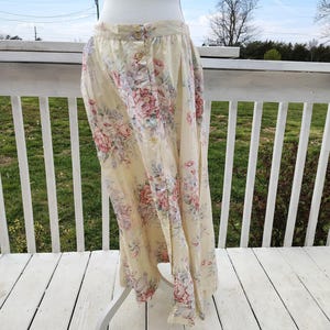 May include: A long, button-down skirt with a floral pattern in shades of pink, purple, and green on a cream background. The skirt has a high waist and is made of a lightweight fabric. The skirt is displayed on a white mannequin.