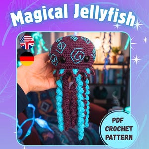 Könnte beinhalten: Ein gehäkeltes Quallen-Spielzeug mit einem lila Körper und türkisfarbenen Tentakeln. Die Qualle hat schwarze Augen und türkisfarbene gestickte Details. Das Bild enthält den Text "Magical Jellyfish" und "PDF Crochet Pattern".