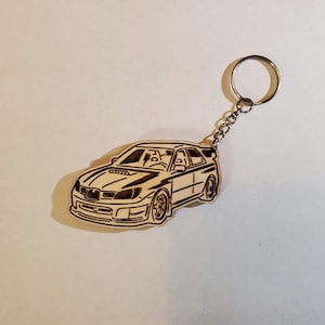 May include: A wooden keychain featuring a black and white outline of a Subaru Impreza WRX.