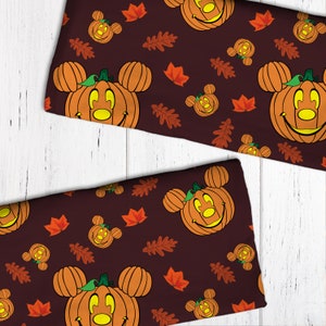 Op de afbeelding: Een bruine stof met een herhalend patroon van oranje jack-o'-lantern Mickey Mouse gezichten en herfstbladeren.