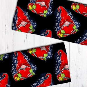 May include: A black fabric with a repeating pattern of gnomes holding red hearts. The gnomes are wearing red hats and have white beards. The background is a dark blue with white hearts.