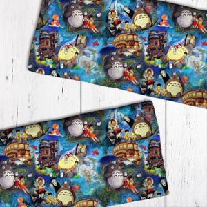 Puede incluir: Una tela azul y blanca con un patrón repetido de personajes de la película animada "Mi vecino Totoro". El patrón incluye a Totoro, el Catbus y otros personajes de la película.