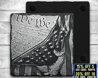 May include: Black and white engraved slate coaster featuring a folded American flag with the words "We the People" from the US Constitution visible in the background. The coaster is made of natural slate and has a rustic look.