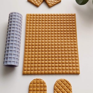 Peut inclure: Un ensemble de pièces en pâte polymère de couleur brune à texture gaufre pour la création. L'ensemble comprend une grande feuille, deux pièces cintrées et trois pièces plus petites. Un rouleau à pâtisserie violet est également inclus.